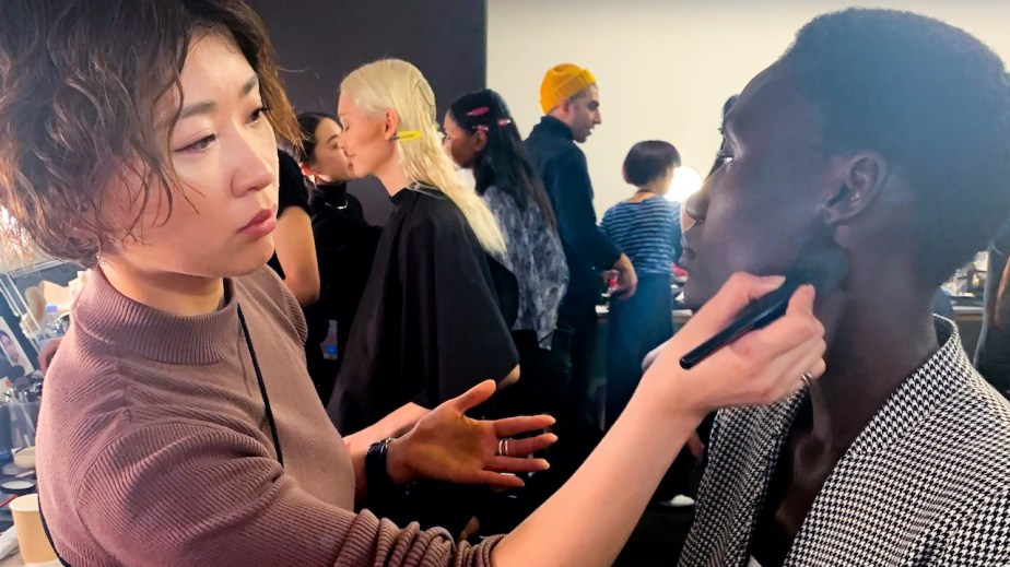 The lead image shows a model getting making done at NYFW.