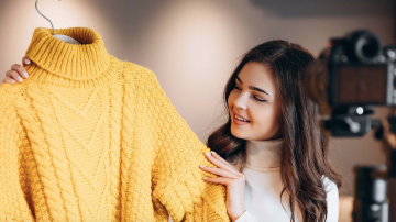 Photograph of a woman holding up a yellow sweater.